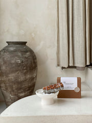 One hand-bound white sage with cinnamon incense bundle resting in a heatproof dish, with its minimalist presentation box behind.