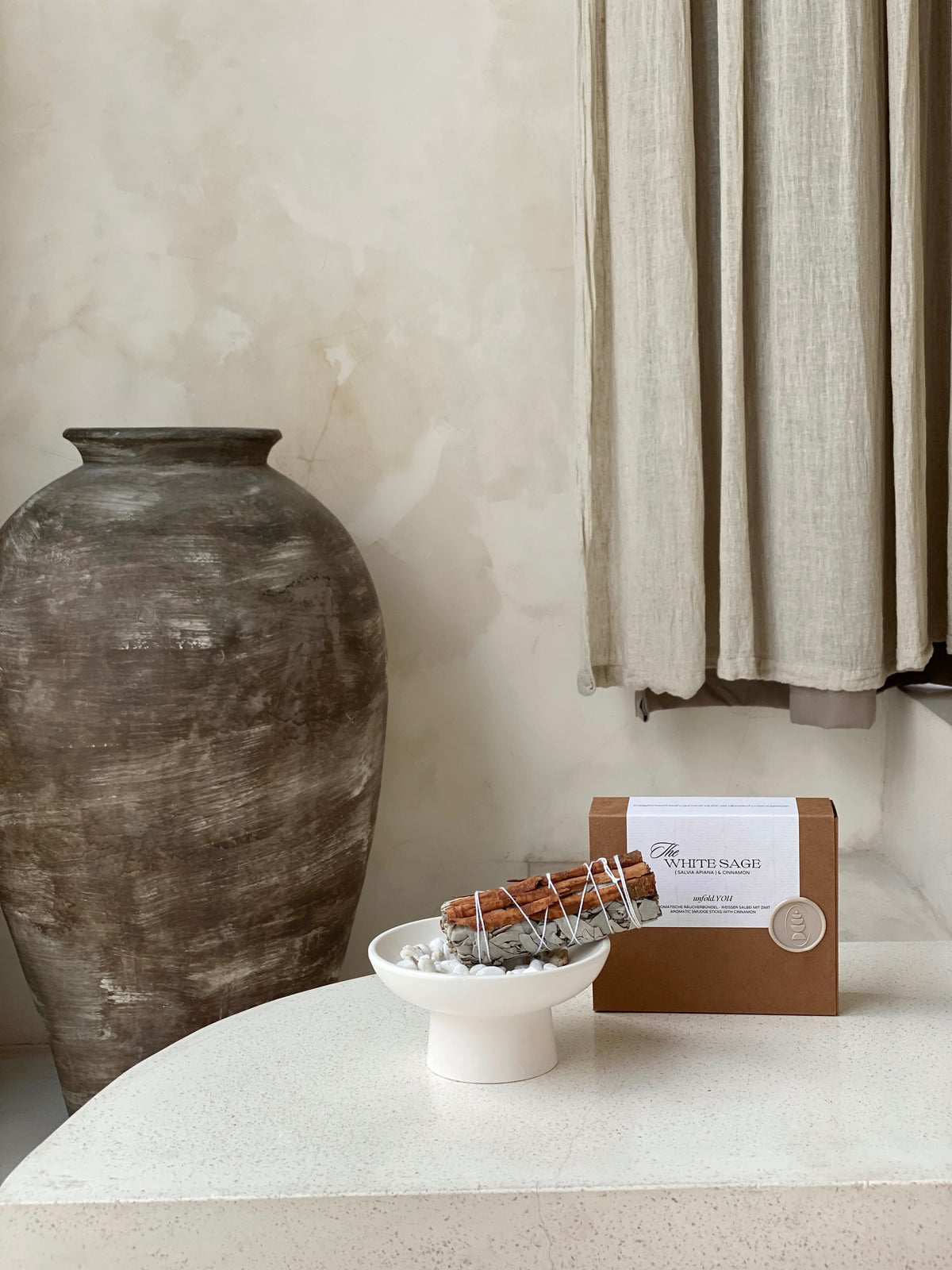 One hand-bound white sage with cinnamon incense bundle resting in a heatproof dish, with its minimalist presentation box behind.