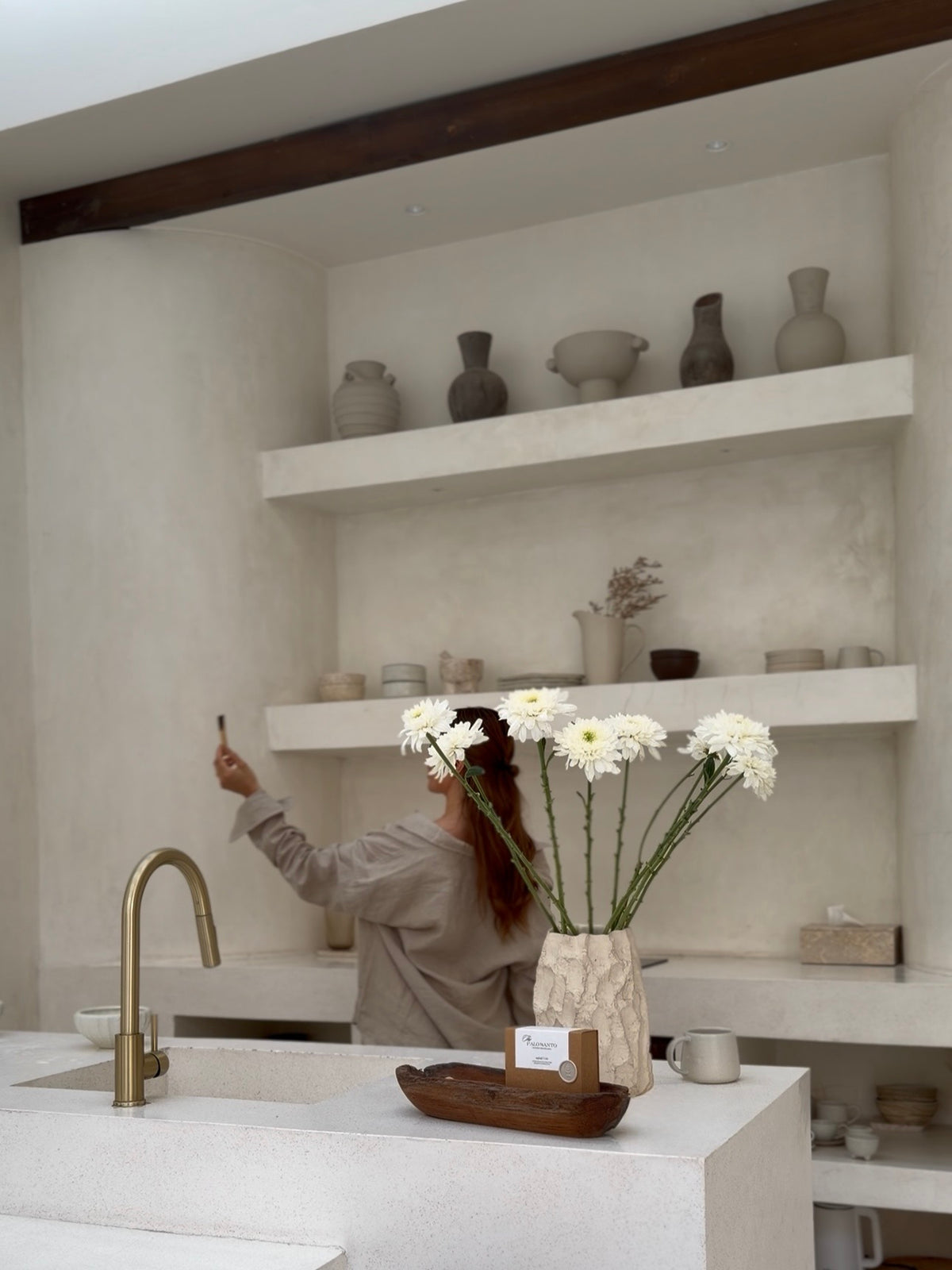 A person gently guiding a smoking Palo Santo stick through a bright, minimalist room to clear the space.
