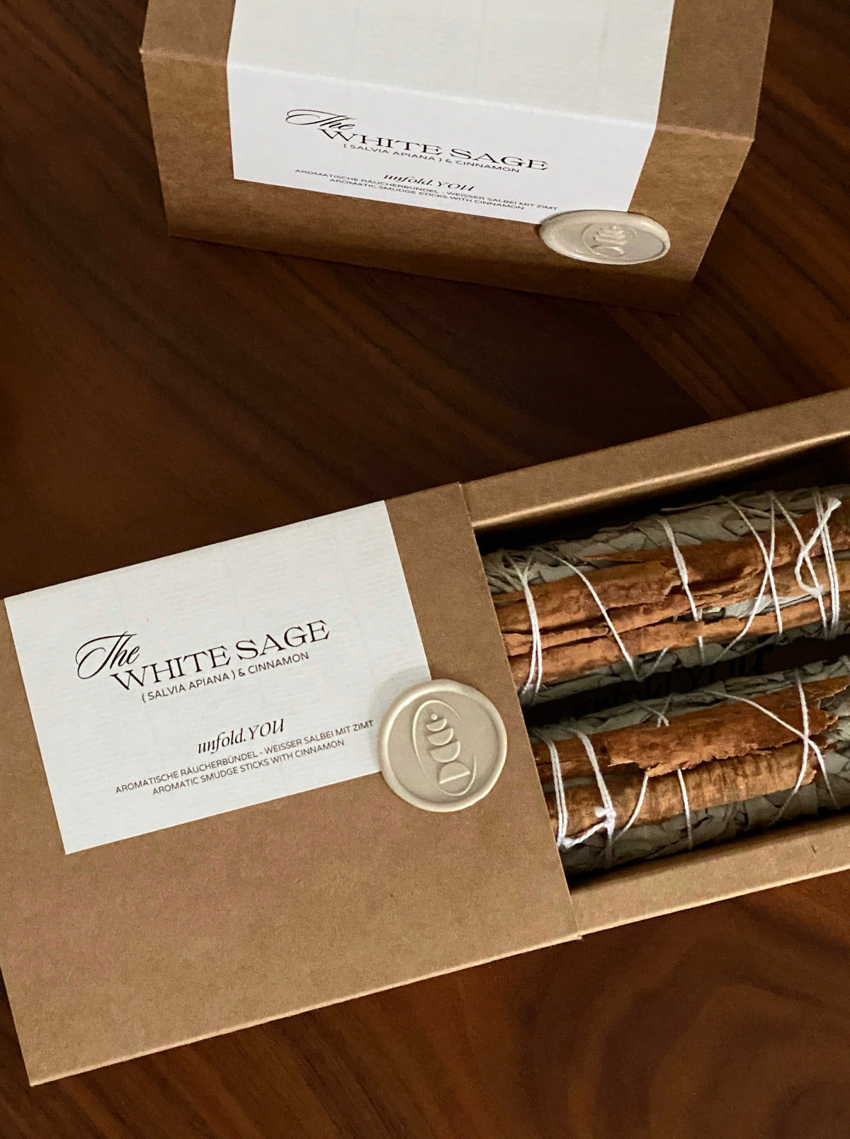 Two hand-bound white sage botanical bundles with whole cinnamon sticks in recyclable craftpaper-box .