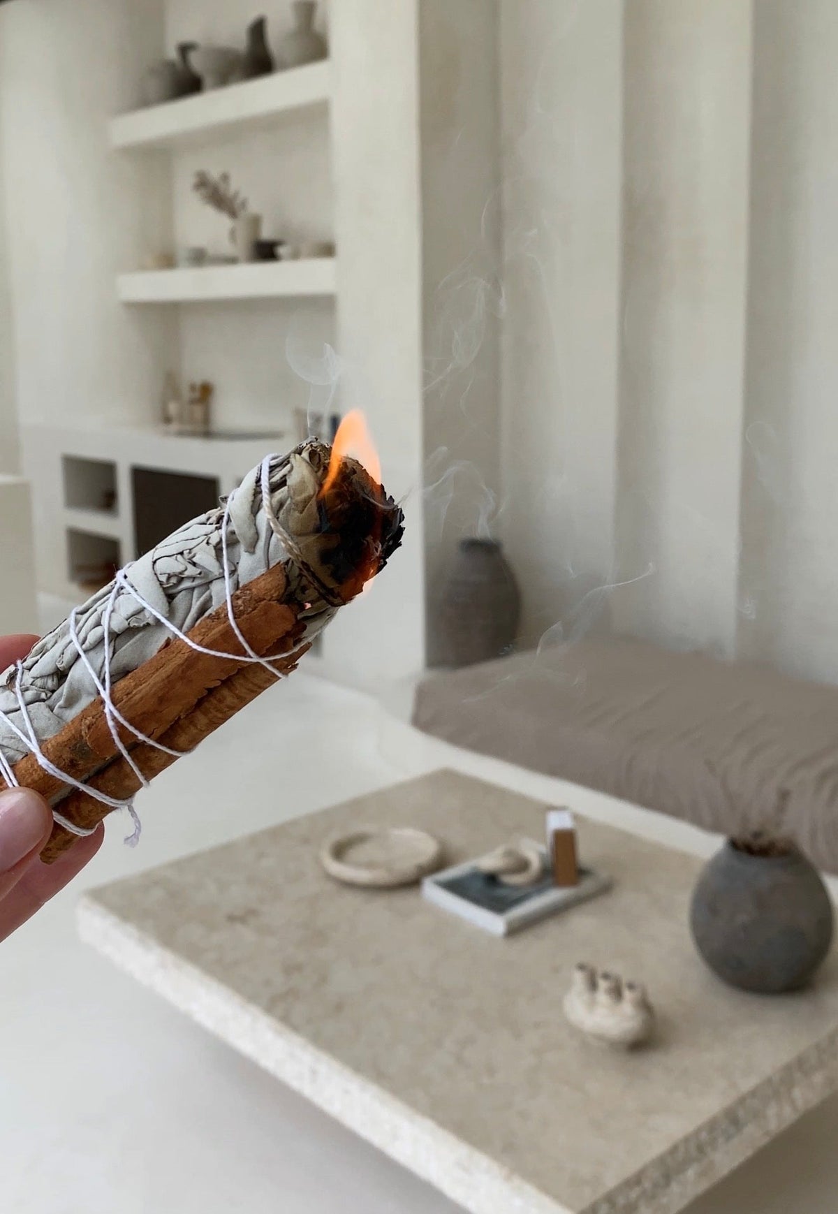 A hand-bound white sage with cinnamon bundle being ignited at a slight angle, with a bright flame catching the tip to release its aromatic botanicals.