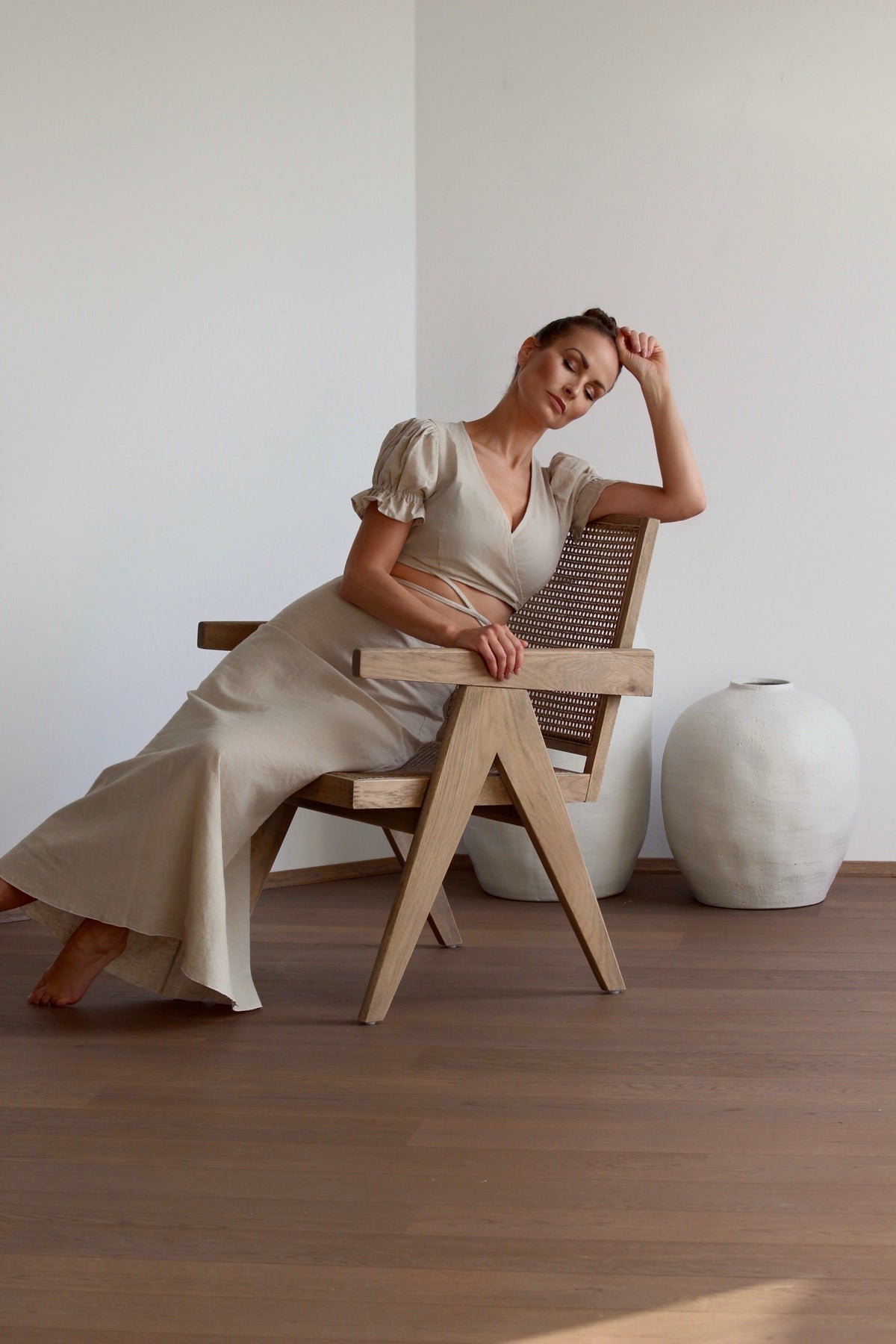 Women sitting on wooden chair wearing alba wrap top made from undyed linen and cotton. Pure elegance